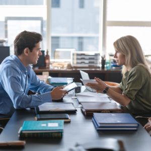 Two groups of professionals are seated at a conference table, engaged in a negotiation over logistics & Carriers documents. Laptops, legal books, and papers are scattered on the table, while the background subtly features transportation elements like cargo ships, airplanes, and trucks. The scene conveys a professional, collaborative atmosphere focused on resolving a dispute. 